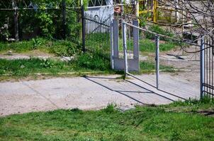 A gate is open in a yard with a fence behind it. The gate is made of metal and is open to the right. The yard is surrounded by a fence and has a lot of grass photo