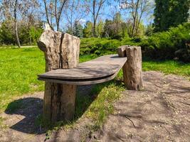 A wooden bench with a tree stump in the middle of it. The bench is in a park with trees in the background photo