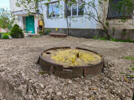 A rusty pipe is sitting on the ground in front of a house. The pipe is old and rusted, and it is surrounded by dirt. The scene gives off a sense of neglect and abandonment, as if the house photo