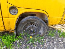 A yellow school bus with a flat tire. The tire is missing and the bus is parked on a dirt road photo
