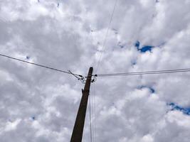 A power line pole is standing tall in the sky. The sky is cloudy and the sun is shining through the clouds photo