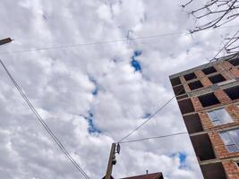 A building with a lot of wires and a cloudy sky in the background. The sky is blue and the clouds are white photo