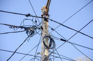 A power line pole with wires hanging from it. The wires are tangled and twisted. The sky is clear and blue photo