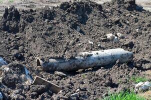 A pipe is laying on the ground in a muddy field. The pipe is covered in dirt and debris, and it is old and rusted. Scene is one of neglect and decay photo