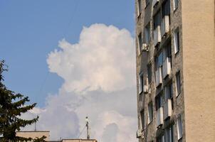 A building with a large cloud in the sky. The cloud is white and fluffy. The building is tall and has many windows photo