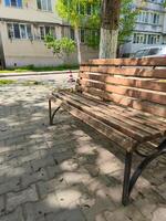 A wooden bench is sitting on a brick sidewalk in front of a building. The bench is empty and the sun is shining on it photo