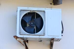 A white air conditioner with a black fan on it. The fan is broken and the air conditioner is not working photo