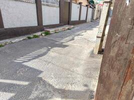 A street with a sidewalk and a fence. The sidewalk is empty and the street is empty. The fence is brown and has a green stripe photo