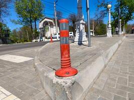 A red and white traffic sign is on the side of a road. The sign is on a cement block and is surrounded by a brick sidewalk. The road is empty and there are no cars or people in the scene photo