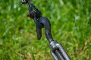 A black and silver chain is hanging from a rope. The chain is attached to a hook and is hanging from a grassy area photo