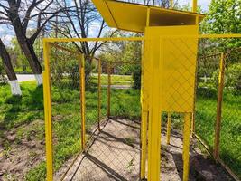 A yellow structure with a fence around it. The fence is made of metal and has a white trim. The structure is empty and he is a shed or a storage unit photo