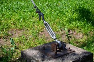 A chain is attached to a metal object on a cement slab. The chain is attached to a rope, which is tied to a tree. The scene is peaceful and serene, with the grass photo
