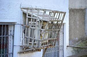A window air conditioner is hanging from a window. The air conditioner is covered in rust and has a cage around it photo