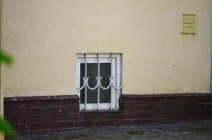 A window with a metal bar on it is on the side of a building. The window is small and has a white frame photo