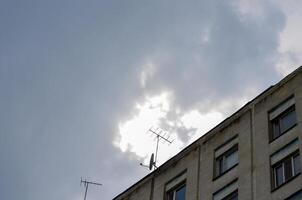 A building with two antennas on the roof. The sky is cloudy and the sun is shining through the clouds photo