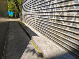 A wall with graffiti on it and a shadow cast on the ground. The wall is made of metal and has a lot of graffiti on it photo