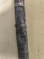 A rusty pipe is leaning against a wall. The pipe is covered in dirt and has a few holes in it photo