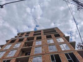 A large brick building with a cloudy sky in the background. The building is under construction and has a lot of windows photo