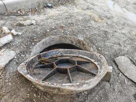A rusty metal object is sitting in a hole in the ground. The object is likely a drain cover or a pipe. The scene is somewhat eerie and abandoned, with the object sitting alone in the dirt photo
