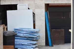 A stack of blue and white boards is piled up next to a closed garage door. The garage door is made of metal and has a black handle. The boards are of different sizes photo