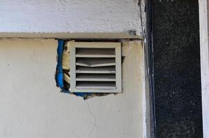 A vent is missing from a wall. The vent is white and has blue trim. The wall is cracked and has a hole in it photo