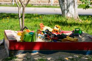 A pile of toys, including a green toy truck, is sitting in a red sandbox. The toys are scattered around the sandbox, with some of them being closer to the front and others towards the back photo