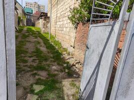 A narrow alleyway with a gate on the right side. The gate is open and the gate is rusted photo