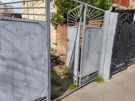 A gate is open and the gate is made of metal. The gate is located in front of a building photo