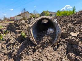 A pipe is laying on the ground in a field. The pipe is broken and has a hole in it. The ground is covered in dirt and rocks. The scene is desolate and abandoned photo