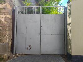 The gray colored gate is closed. The gate is made of metal and is located in front of the building photo