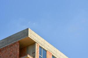 A brick building with a cement roof and a blue sky in the background. The building is unfinished and has a lot of windows photo