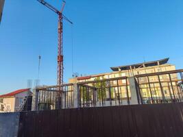 A crane is lifting a large object in front of a building. The sky is clear and blue photo