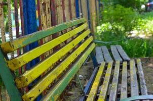 A bench with yellow and green stripes sits in a park. The bench is old and worn, but it still has a certain charm to it. The colors of the bench are bright and cheerful photo