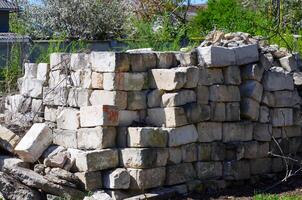 A pile of bricks is stacked in a corner of a yard. The bricks are old and worn, and the pile is quite large. The scene gives off a sense of abandonment and neglect photo