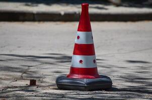 A red and white cone with black dots on it is sitting on the ground. The cone is a traffic cone and is placed in the middle of the road photo