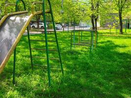 A park with a slide and a set of monkey bars. The slide is green and the monkey bars are silver. The park is empty and the grass is green photo
