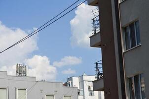 A building with a balcony and a cell phone tower in the background. The sky is blue with some clouds photo