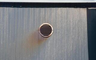 A vent is on the wall of a building. The vent is rusty and has a hole in it photo