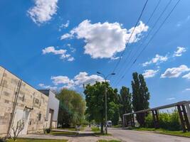A street with a building in the background and a tree in the foreground. The sky is blue and there is a cloud in the sky photo
