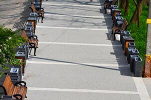 A row of benches and trash cans on a sidewalk. The benches are lined up in a row, with some of them empty. The scene gives off a sense of order photo