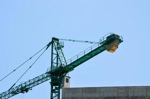 A crane is lifting a large object. The crane is green and is located in the sky. The sky is clear and blue photo