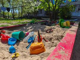A pile of toys and plastic cups are scattered on the sand in a park. The scene is messy and disorganized, with no clear purpose or direction. Scene is chaotic and unkempt photo