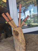 A wooden block with five wooden knives on top of it. The knives are arranged in a way that they look like they are standing upright. The block is placed on a stone surface photo