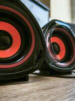 Two speakers with red and black accents sit on a wooden table. The speakers are black and red, and they are placed on a wooden surface photo