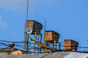 Three rusty metal tanks are on top of a building. The tanks are connected to a power line photo