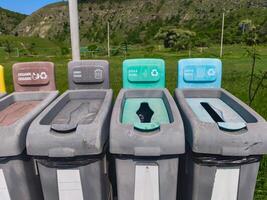 A row of trash cans with different colored lids and signs on them. The trash cans are labeled for different types of waste, such as glass, paper, and plastic photo