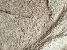 A wall with a rough texture and a few cracks. The wall is made of cement and has a grey color photo
