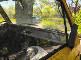 A yellow car with a dirty windshield and a person in the back. The car is parked in a field photo
