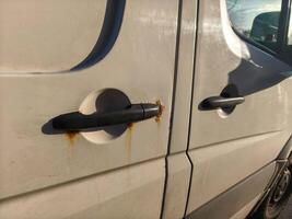 The door of a van has a rusty handle. The handle is black and the door is white photo