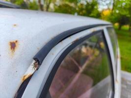 A car with a rusted bumper and a broken window. The car is parked in a grassy area photo